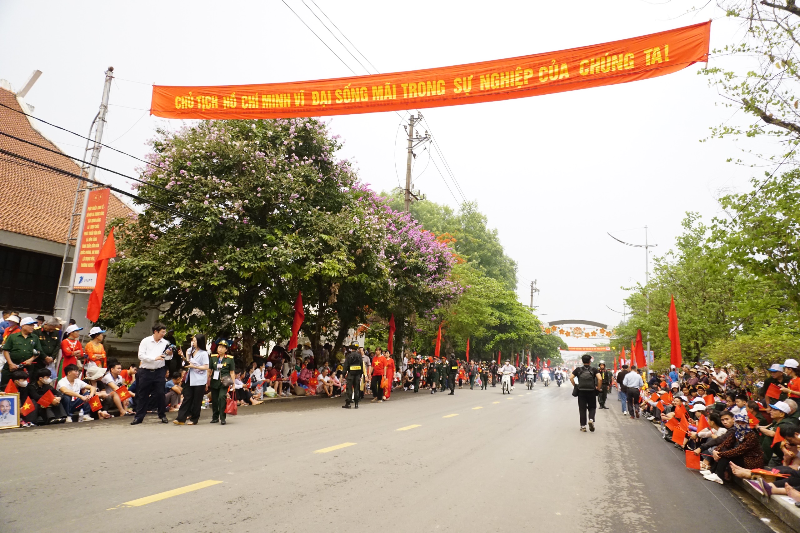 People stands in the rain to watch the military march and parade on the streets of Dien Bien Phu